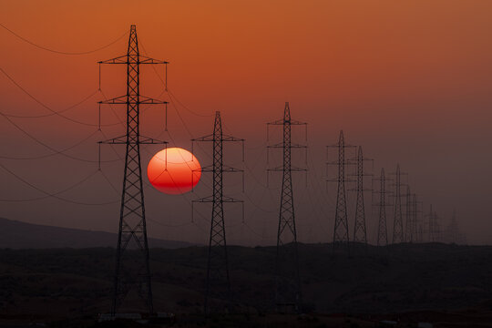 View of stark power lines cutting across the horizon as the sun sinks, painting the sky with fire, contrasting industrial presence with natural beauty, Rub' al-Khali, United Arab Emirates.