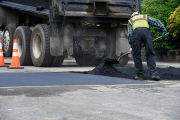 Construction worker on roadworks paving repair project using shovel to move freshly dumped hot asphalt from dump truck  © knelson20