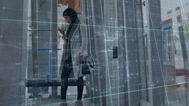 Woman commuter checking transit app and tapping phone in glass stop as digital grid spanning glass
