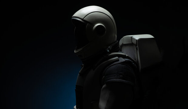A close-up silhouette of an astronaut in a textured suit and helmet against a dark background