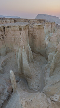 Aerial view of the stark, sun-baked yardangs rise from the desert floor, their pale forms contrasting with the dusky sky, Shahdad, Kerman Province, Iran.