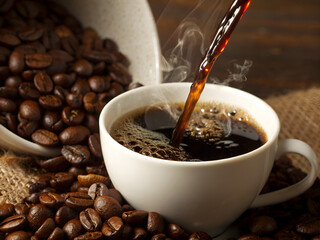 A warm cup of coffee in a white ceramic mug, surrounded by scattered roasted coffee beans, with soft natural lighting.