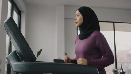 A Muslim woman in a hijab exercising on a treadmill in a modern gym, promoting health and fitness