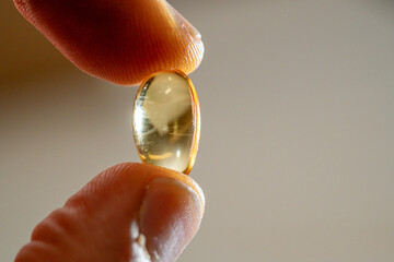 Omega-3 capsule tablet placed between the thumb and index finger in macro photography.