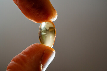 Omega-3 capsule tablet placed between the thumb and index finger in macro photography.