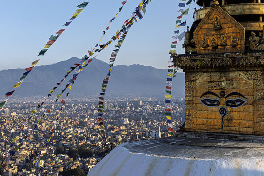 View of prayer flags flutter from the ancient stupa, its golden spire watching over the sprawling cityscape below, nestled against distant mountains, Swayambhunath, Bagmati Province, Nepal.