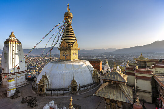 View of the Swayambhunath Stupa gleams with gold under a clear sky, prayer flags flutter in the breeze above the temple, Swayambhunath, Bagmati Province, Nepal.