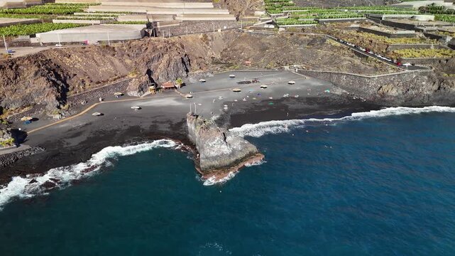 Dynamic aerial drone orbit shot over Charco Verde Beach, showcasing the rugged volcanic coastline and black sand of La Palma, Canary Islands, Spain.