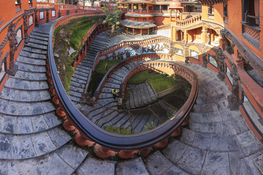 View of serpentine stairs, adorned with red railings, spiraling down into a verdant courtyard, creating a mesmerizing architectural dance, Pokhara, Gandaki Province, Nepal.
