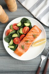 Piece of tasty grilled salmon, lemon, rosemary and salad served on grey wooden table, flat lay