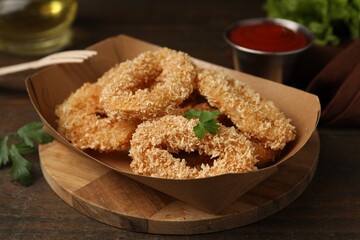 Deep fried squid rings with parsley in takeaway paper box on wooden table, closeup