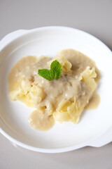 Roti jala with creamy durian coconut sauce on a white plate