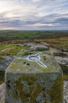 View of a moss-covered triangulation pillar, its metallic top glinting against the muted colors of the landscape, overlooking the distant green fields, Bodmin, England, United Kingdom.