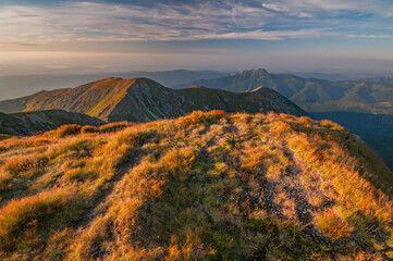 View of golden light warms the high-altitude grasses, casting long shadows across the rugged mountain terrain under a vast sky, Bobrovec, Zilina Region, Slovakia.