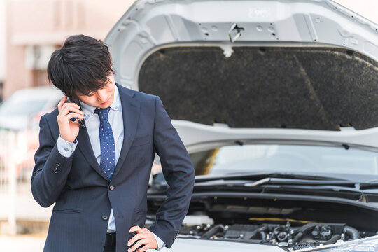 Young Asian man calling on smartphone in front of car (road service, trouble, rescue, trouble)

