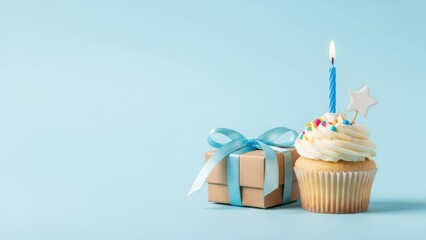 Single blue birthday cupcake with lit candle and small gift box wrapped with blue ribbon on light blue background, perfect for celebration or party announcement with copy space