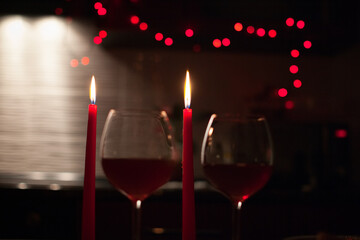 Two red wine glasses with lit candles behind, warm bokeh lights and romantic mood. g.