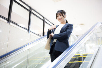 空港や駅のエスカレーターを降りるスーツ姿のキャリア女性のビジネス移動シーン