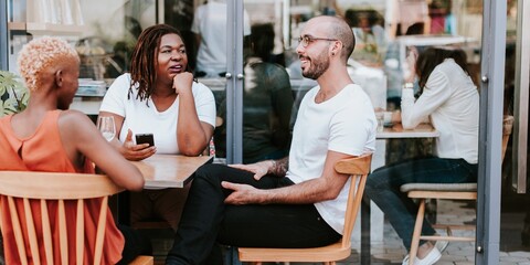 Group of diverse people sitting at a cafe table, chatting and smiling. Casual outdoor setting with diverse individuals enjoying a conversation and drinks. Diverse friends at cafe outdoor.