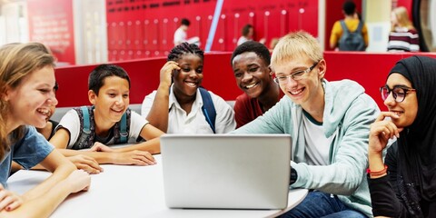 Diverse group of exchange students smiling with a laptop. Teens of various ethnicities engaged in learning. Happy students learning in a school setting. Exchange students learning at working together.