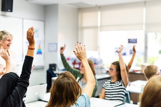 Students in classroom raising hands, engaging in learning. Diverse group of students participating. Classroom setting with teacher guiding students. Students raising hands and asking questions. - Powered by Adobe