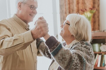 Elderly friends dancing happily indoors. Smiling seniors enjoying a dance. Joyful elderly pair sharing a moment. Senior friends embracing dance and happiness. Happiness and joy at old age.
