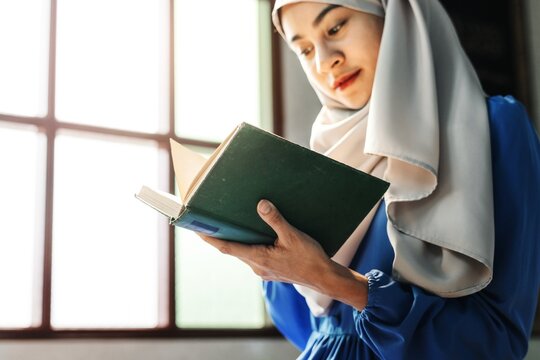 A young Muslim woman in a hijab reads a book thoughtfully. This Muslim woman enjoys reading, showcasing her love for literature and knowledge in a serene environment.