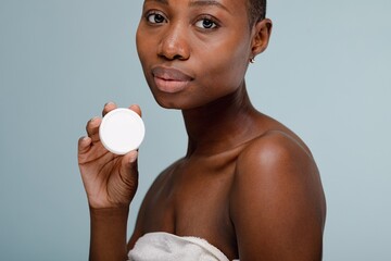 Person holding a round container, wrapped in a towel. Skincare focus with a neutral background....
