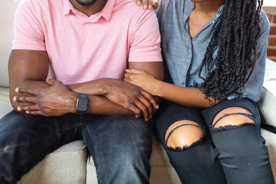 Close-up of African American couple sitting on a couch, showing their arms and torsos showing empathy and support. Emotional support and empathy are key themes.