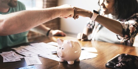 Two people fist bump over table with a piggy bank, teamwork and savings. Diverse man and woman fist bump on financial planning. Couple fist bump teamwork on financial, accounting and investment topic