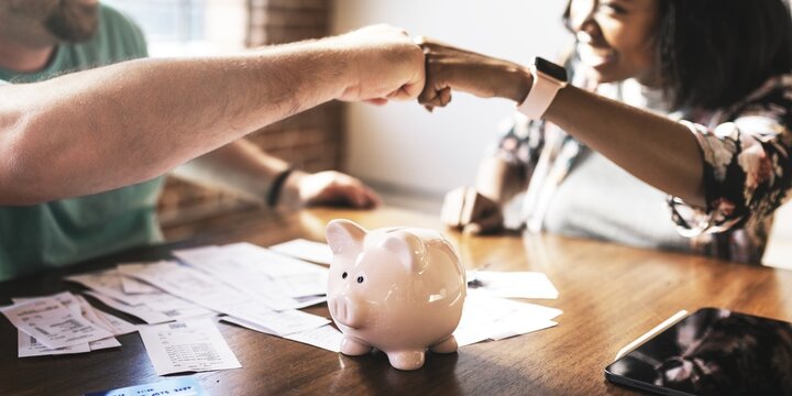 Two people fist bump over table with a piggy bank, teamwork and savings. Diverse man and woman fist bump on financial planning. Couple fist bump teamwork on financial, accounting and investment topic - Powered by Adobe