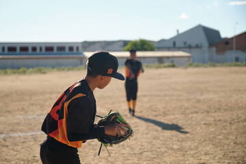 Boy baseball player holding ball and glove, another player on field in background