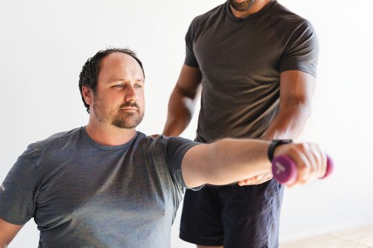 A man exercises with a dumbbell, assisted by a trainer. The man focuses on lifting, while the trainer guides. Exercise, fitness, and training are key themes. Workout exercise concept photography. - Powered by Adobe