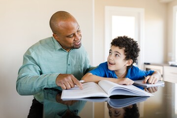 African American man teaching his white child homework. Father teach his son homework. Father and son enjoying a learning moment together at home. Homeschooling and learning concept. Father teach son