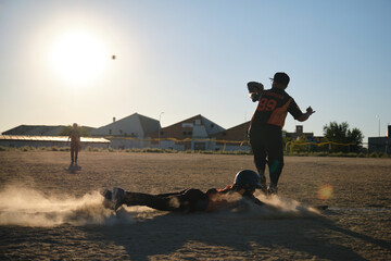 Baseball player sliding headfirst into base, creating a cloud of dust during game
