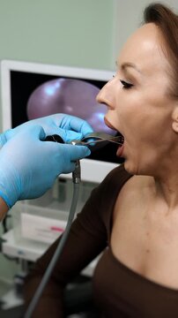 Close up of an ENT doctor performing a throat endoscopy examination on a patient using a medical endoscope and metal tongue depressor in a modern clinic during diagnostic procedure.
