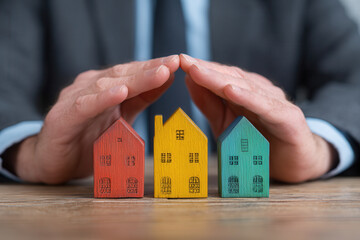 Protecting investments with colorful wooden houses under a businessman's hands in an office setting
