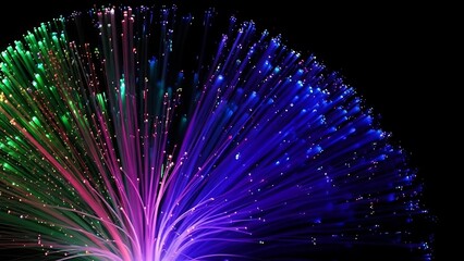 Close up of fiber optic strands glowing in green pink and blue against a dark black background