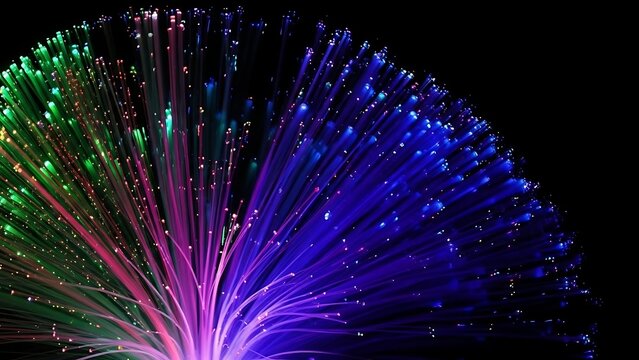 Close up of fiber optic strands glowing in green pink and blue against a dark black background