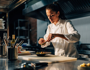Chef garnishing a dish in commercial kitchen, food preparation, gourmet cooking, culinary arts, restaurant work, chef attire, fine dining experience.