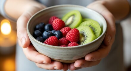 Close-up of hands holding a bowl of fresh berries and kiwi slices.