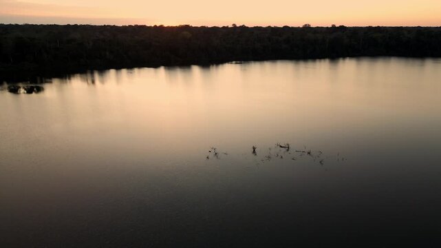 Drone video of Lake Valencia at sunset, featuring smooth aerial views of golden reflections, tropical rainforest landscape, and serene Amazonian atmosphere in Madre de Dios, Peru.