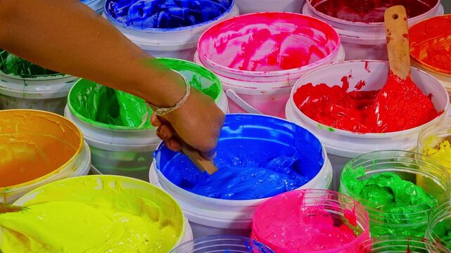 Scoop of Blue Plastisol Ink from a White Bottle for Fabric Prints. A vivid assortment of paint containers filled with bright pigments, showcasing texture, richness, and the beauty of mixed colors.