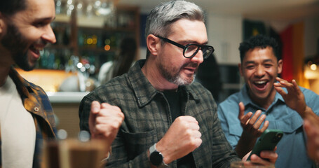 Phone, cheering and men in pub for sports game with goal, victory or winning championship. Happy, cellphone and group of male friends with celebration for watching football match in bar together.