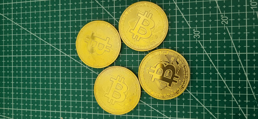Four golden Bitcoin coins arranged on a green grid mat, symbolizing cryptocurrency and digital finance.