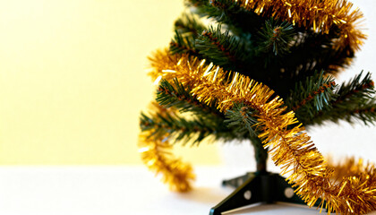 Small artificial Christmas tree wrapped in gold tinsel against a simple two-tone background.