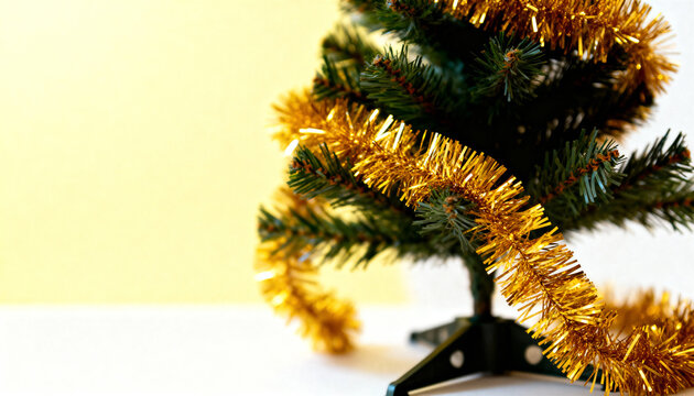 Small artificial Christmas tree wrapped in gold tinsel against a simple two-tone background. - Powered by Adobe