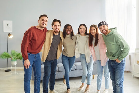 Cheerful diverse friends hanging out together. Group portrait of happy smiling young multiracial people in casual clothes posing for picture in living room in modern apartment. Friendship concept