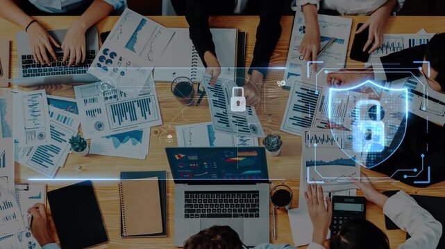 A collaborative business meeting featuring laptops, documents, and digital security symbols. Professionals analyze data and plan strategies in a modern workspace environment. Raster