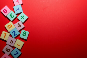 A vibrant red background, dominating most of the frame, features a cluster of small square rubber tiles or erasers with numbers (0-9) and mathematical symbols (addition, subtraction, multiplication, d
